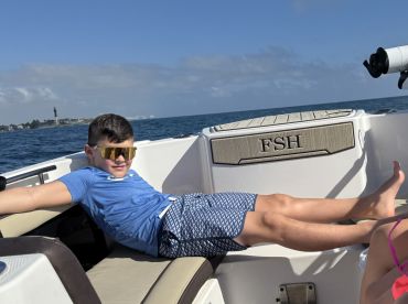 A young boy relaxes on the deck of a boat, enjoying a sunny day on the water — perfect for family outings and summer adventures.