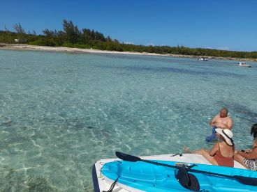 A group enjoys a sunny day at the beach, relaxing on a kayak and swimming in the crystal-clear waters — perfect for a fun day out on the water.