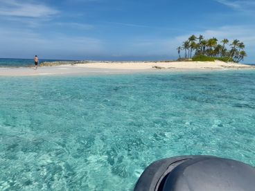 A serene view of a man walking along a pristine beach on a tropical island, with crystal-clear waters inviting for a swim — a perfect getaway for beach lovers.