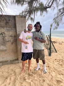 Two individuals pose together on a sandy beach, capturing a moment of camaraderie.
