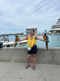 A woman joyfully interacts with two colorful parrots at the marina, showcasing a delightful wildlife experience perfect for nature lovers.
