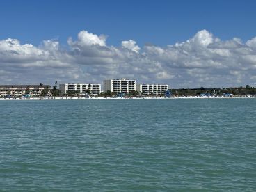 A picturesque view of a beach with people enjoying the sun and sand, framed by beautiful coastal buildings under a bright blue sky.