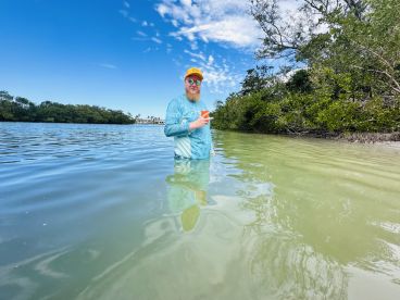 A man stands in shallow water surrounded by mangroves, enjoying a scenic day in nature — perfect for eco tours and wildlife exploration.