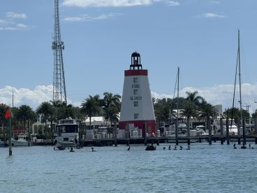 A picturesque view of the Faro Blanco lighthouse at a marina, surrounded by boats and palm trees, showcasing a beautiful day on the water.