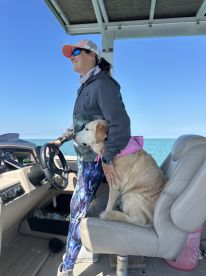 A woman enjoys a sunny day at the helm of a boat with her dog by her side, showcasing a cozy interior space perfect for leisurely outings on the water.