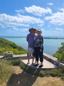A couple poses for a photo against a stunning ocean backdrop, capturing a memorable moment during their vacation in a picturesque location.