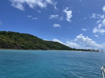 A stunning view of a lush green coastline under a bright blue sky, showcasing the natural beauty of the island — perfect for eco tours and scenic boat trips.