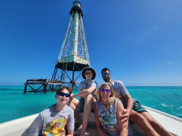 A cheerful family poses on their boat with a historic lighthouse in the background, enjoying a sunny day on the vibrant ocean — perfect for family adventures and sightseeing.