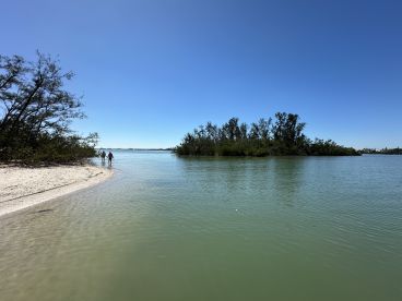 A couple strolls along a sandy beach, surrounded by lush greenery and calm waters, showcasing the serene beauty of a coastal escape.