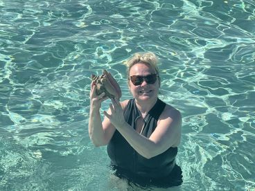 A woman joyfully holds a conch shell while swimming in crystal-clear waters, showcasing a unique marine encounter.