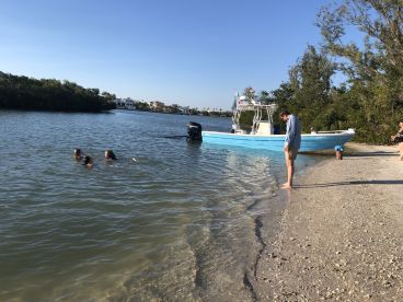A group enjoys a fun day at the beach, swimming near a boat anchored in the shallow waters — perfect for family outings and water adventures.