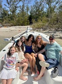 A joyful group of family and friends relaxes on a boat, enjoying a sunny beach day — perfect for creating lasting vacation memories.