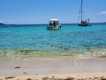 A picturesque view of two boats anchored in clear turquoise waters, with a swimmer enjoying the beach — a perfect setting for a relaxing day on the water.
