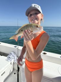 A young girl proudly holds up her catch while fishing on a boat, showcasing a vibrant fish against a beautiful ocean backdrop — a perfect moment for family fishing adventures.