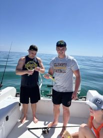 Two friends proudly display their catch while fishing on a boat, enjoying a sunny day on the ocean — a perfect snapshot of a fun fishing trip.