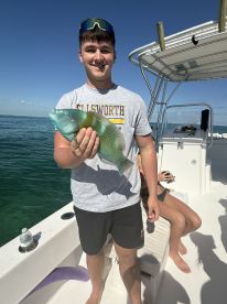 A teenager proudly displays his catch while fishing on a boat, showcasing the excitement of a successful day on the water.