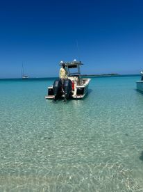 A person stands on a boat anchored in crystal-clear waters, with a picturesque island in the background — a perfect scene for a day of exploration and relaxation.