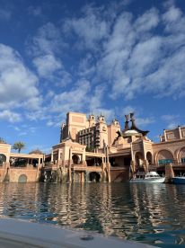 A stunning view of the Atlantis resort from the water, showcasing its unique architecture against a backdrop of blue skies and reflective waters — a perfect destination for luxury vacations.