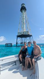 A family poses for a fun photo on their boat with a stunning lighthouse in the background, capturing a memorable moment in the beautiful turquoise waters.