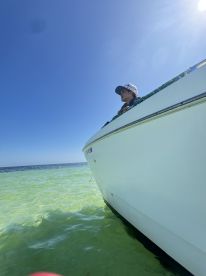 A young person enjoys the view from the side of a boat, surrounded by clear green waters — a perfect moment for relaxation on a sunny day.