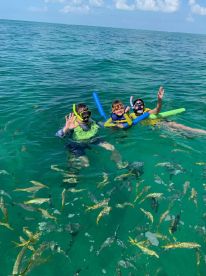 Three kids enjoy snorkeling in clear waters, surrounded by fish — a perfect family adventure in the ocean.