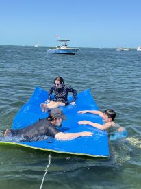 A family enjoys a fun day on the water, playing on a floating mat while swimming and relaxing under the sun — perfect for summer adventures.