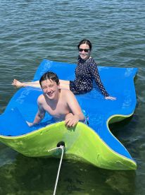 A boy and girl enjoy a sunny day on a floating mat in clear waters, capturing the essence of summer fun and aquatic adventures.
