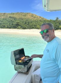 A man enjoys grilling fresh food on a boat, showcasing the perfect amenities for a fun day on the water. Ideal for those looking to combine boating with culinary experiences.
