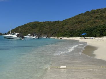 A picturesque beach scene featuring several boats anchored near the shore, with guests enjoying the sun and water — perfect for a relaxing sandbar stop.