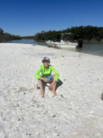 A young boy enjoys a day at the beach, playing with a fishing rod near a boat anchored in the background — a perfect family adventure in nature.