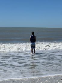 A young boy enjoys a peaceful day of fishing at the beach, standing in the gentle surf with the vast ocean in the background — a perfect family-friendly outdoor activity.