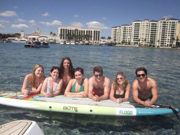 A lively group of friends enjoys a sunny day paddleboarding in clear waters, capturing the essence of summer fun and beach adventures.