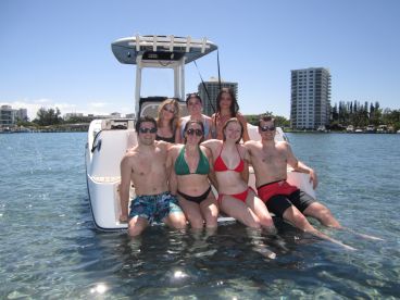 A cheerful group of friends poses on a boat in shallow water, enjoying a sunny day out on the water — perfect for summer adventures and memorable outings.