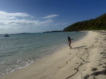 A young girl walks along the sandy beach, enjoying the serene waters and nearby boats — a perfect snapshot of a fun day by the sea.
