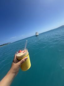 A refreshing cocktail is held up against a stunning backdrop of turquoise waters and a yacht in the distance, perfect for enjoying a day on the water.