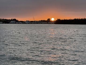 A stunning sunset casts a warm glow over the water, creating a picturesque scene along the coastline — perfect for evening boat cruises.