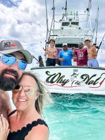 A joyful group poses for a selfie in front of the fishing boat 'Why Nat,' capturing a fun day on the water with friends and family.