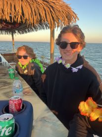 Two young guests enjoy a festive moment on a boat, adorned with leis and drinks, perfect for a fun day on the water.