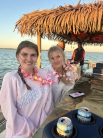 Two friends enjoy a festive moment on a boat, adorned with leis and drinks, capturing the essence of celebration on the water.