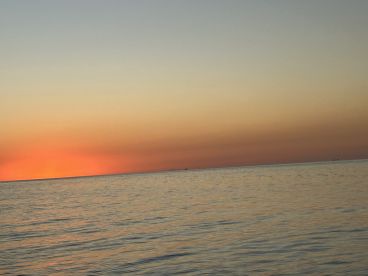 A serene sunset over calm waters, creating a beautiful gradient of colors in the sky. Ideal for capturing the tranquil essence of a boating experience.