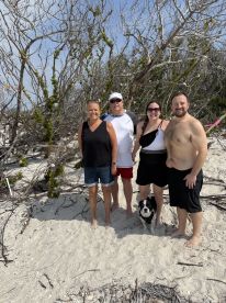 A cheerful group poses on the beach with their dog, surrounded by nature — perfect for family outings and beach adventures.