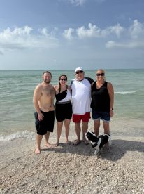A cheerful group of friends poses together on the beach with their dog, capturing a memorable moment by the water.