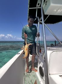 A fisherman proudly displays a freshly caught lobster aboard a boat, showcasing the thrill of ocean fishing and the beauty of the surrounding waters.