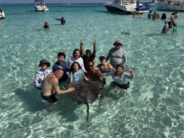A lively group interacts with a stingray in shallow waters, creating unforgettable memories during their aquatic adventure.