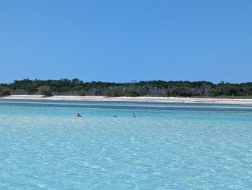 Two individuals enjoy a refreshing swim in the clear turquoise waters near a sandy beach, perfect for a relaxing day in the sun.