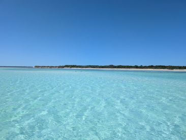 A stunning view of a clear turquoise lagoon with a distant beach, showcasing a perfect day for swimming and relaxation.