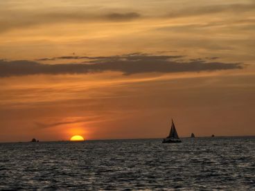 A serene sunset view featuring a sailboat silhouetted against the vibrant orange sky, perfect for capturing the beauty of evening cruises.