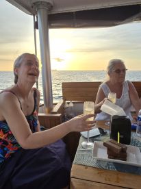Two women enjoy a sunset celebration on a boat, toasting with cocktails and sharing a dessert — a perfect moment for special occasions on the water.