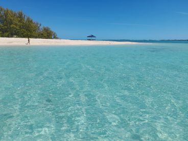 A serene view of a beach with a person walking along the shore, showcasing the stunning turquoise waters and sandy landscape — a perfect destination for relaxation and exploration.