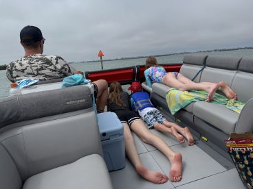 A group of children and an adult enjoy a relaxing moment on a boat, peering over the edge while taking in the scenery — a perfect family outing on the water.
